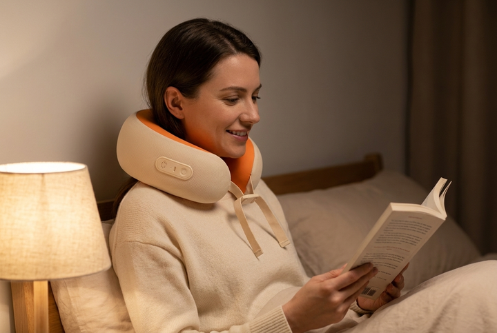 Woman wearing the U-shaped neck massager reading in bed