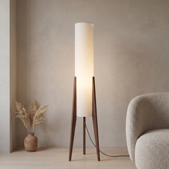 Walnut tripod floor lamp with a white fabric cylinder shade glowing softly in a living room