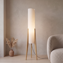 Oak tripod floor lamp with a white fabric cylinder shade glowing softly in a living room