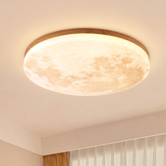 Light wood rim moon ceiling light glowing warm on a bedroom ceiling