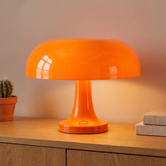 Orange retro mushroom table lamp lit on an oak sideboard beside books and a cactus