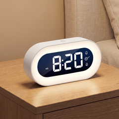 White digital alarm clock with a glowing night light ring on a wooden bedside table