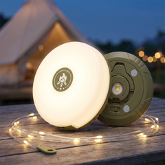 Round camping lantern lit warm on a wooden camp table with its string light coiled beside it at dusk