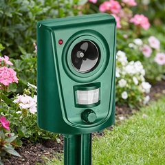 Green ultrasonic cat repeller staked in a flower border beside a lawn