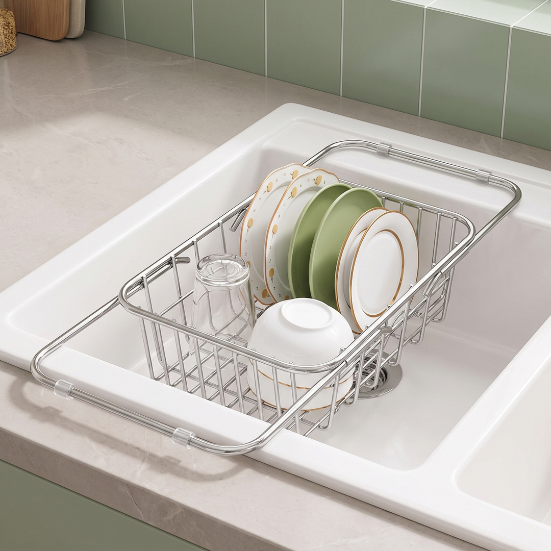 Expandable stainless steel dish drainer resting across a white kitchen sink with plates, a bowl and a glass