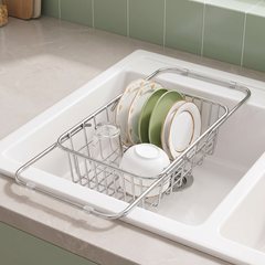 Expandable stainless steel dish drainer resting across a white kitchen sink with plates, a bowl and a glass