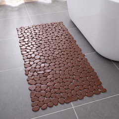 Brown pebble shower mat on a grey tiled bathroom floor beside a bath