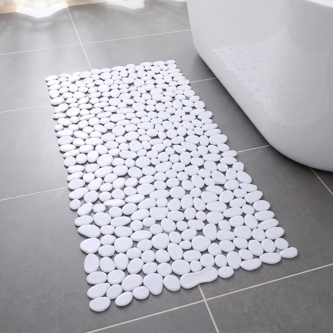 White pebble shower mat on a grey tiled bathroom floor beside a bath