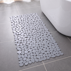Grey pebble shower mat on a grey tiled bathroom floor beside a bath