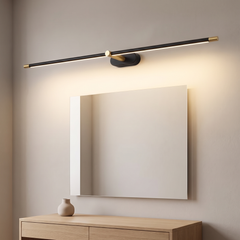 Slim black wired LED over mirror light with brass end caps glowing warm above a mirror