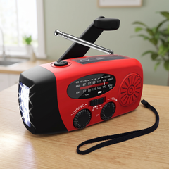 Red wind up radio with hand crank, aerial and lit torch on a wooden table