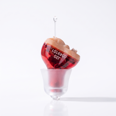 Red right ear in-ear hearing amplifier with a soft frosted eartip on cream travertine