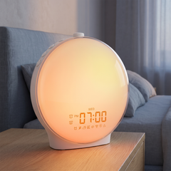 Round full-screen sunrise alarm clock glowing warm orange on an oak bedside table at dawn