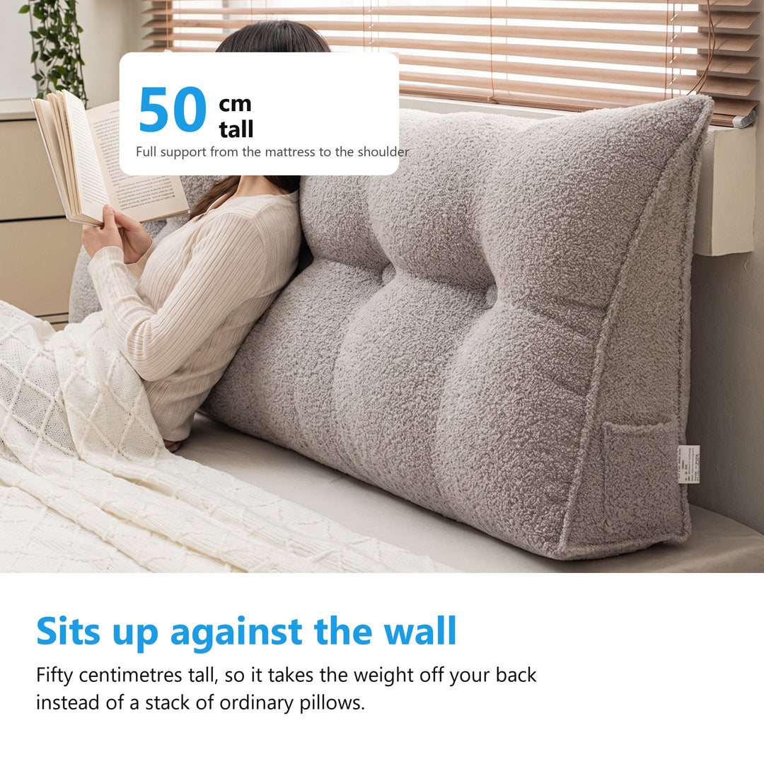 Woman sitting up in bed reading a book against a triangle headboard cushion