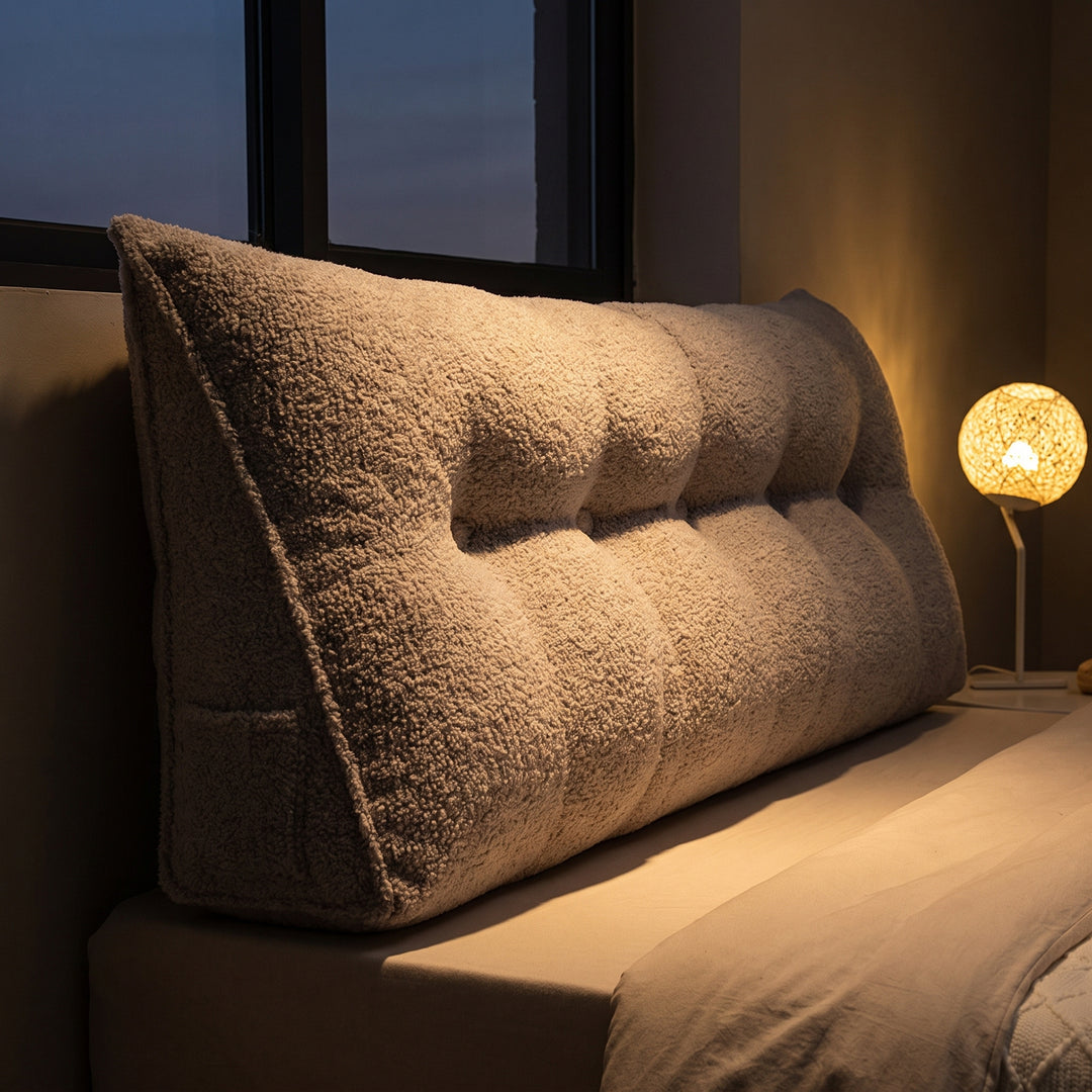Headboard bolster cushion on a bed at dusk with a bedside lamp glowing