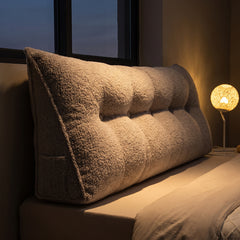 Headboard bolster cushion on a bed at dusk with a bedside lamp glowing