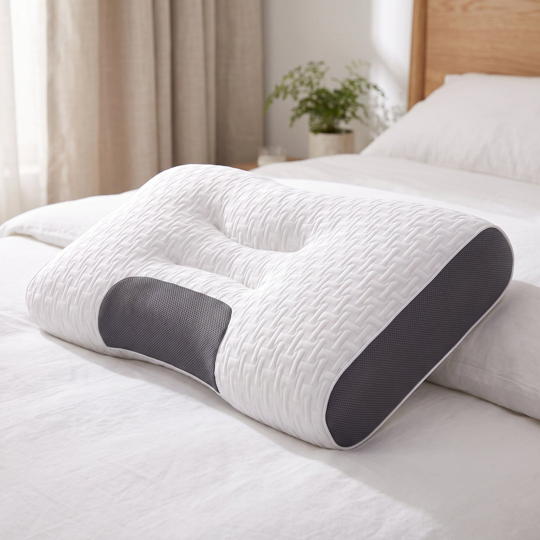 Contoured cervical support pillow with a white woven knit cover, charcoal grey mesh panels and a centre channel, on a made bed in a bright bedroom