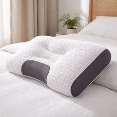 Contoured cervical support pillow with a white woven knit cover, charcoal grey mesh panels and a centre channel, on a made bed in a bright bedroom