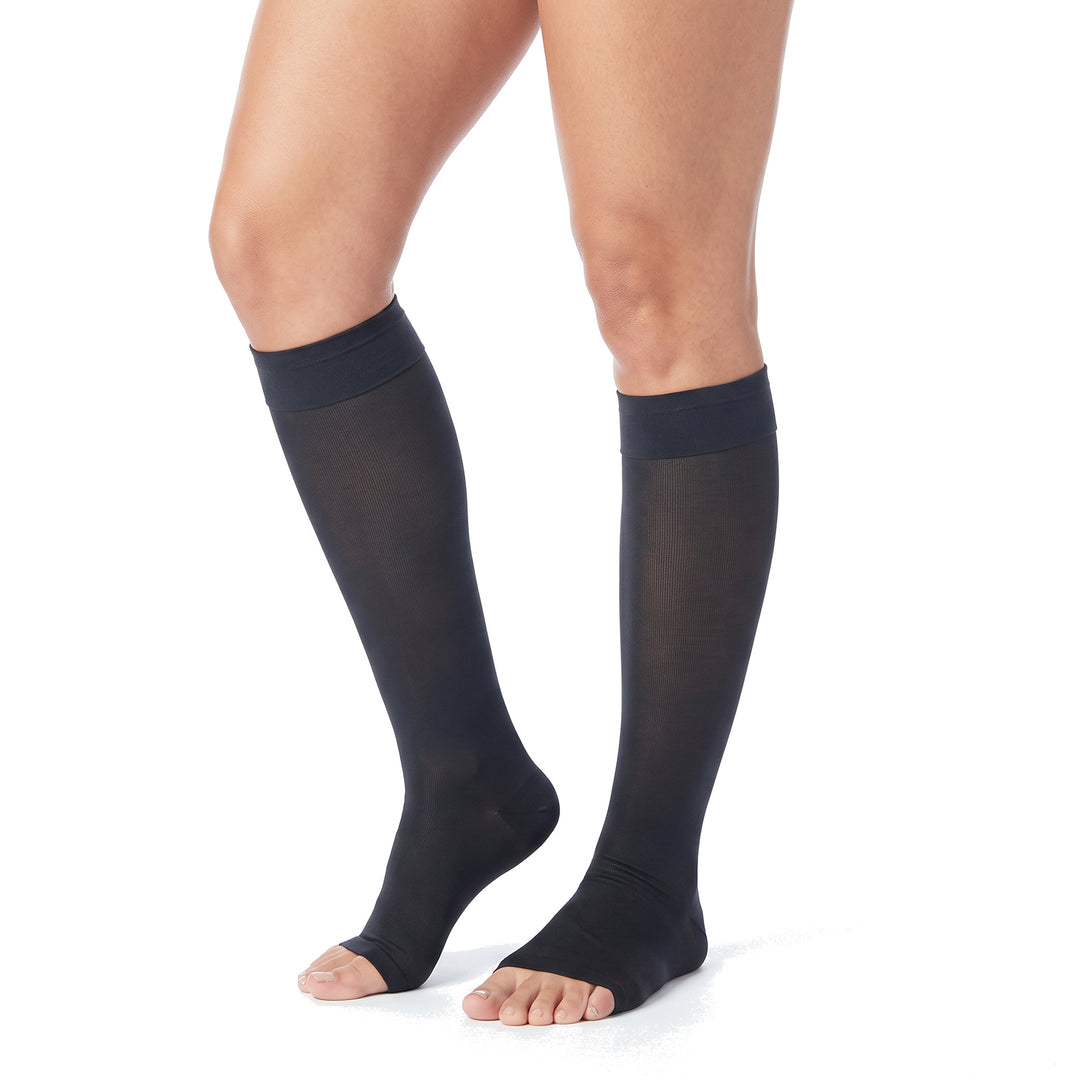 Legs wearing black knee high open toe compression stockings on a white background