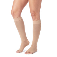 Legs wearing skin tone knee high open toe compression stockings on a white background