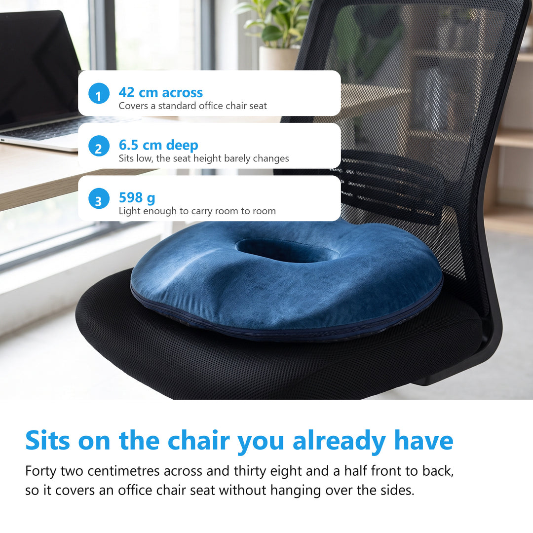 Navy donut cushion sitting flat on the seat of a black mesh office chair at a bright desk