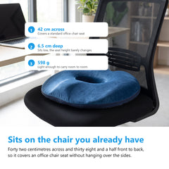 Navy donut cushion sitting flat on the seat of a black mesh office chair at a bright desk