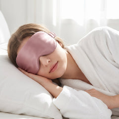 Woman fully clothed in a robe asleep wearing a pink silk eye mask correctly over both eyes