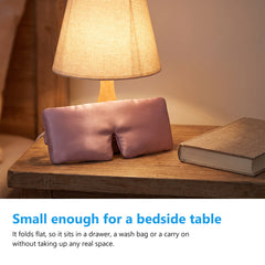 Silk eye mask resting on a bedside table next to a lamp and a book