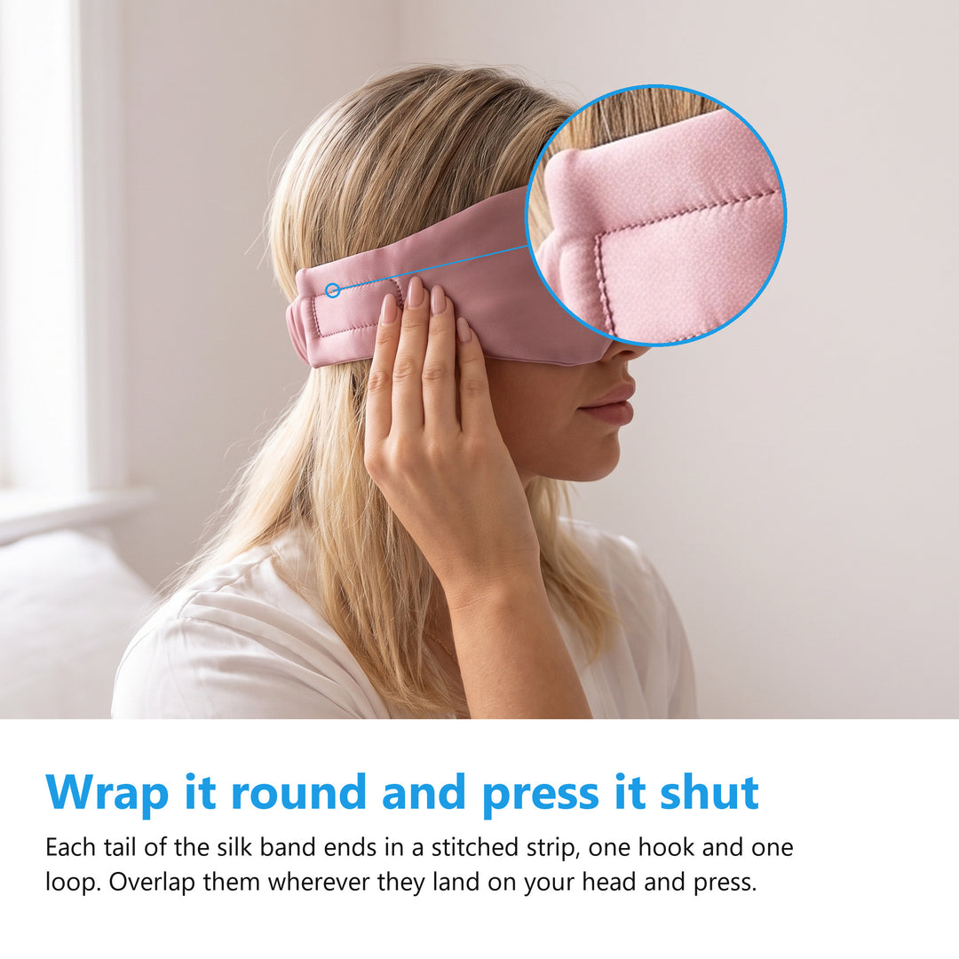 Woman wearing a pink silk eye mask pressing the hook and loop strip on the band tail shut at the side of her head