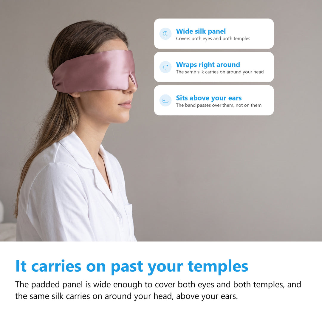 Side view of a woman wearing a pink silk eye mask, the wide padded panel covering both temples and the band running around her head above her ear