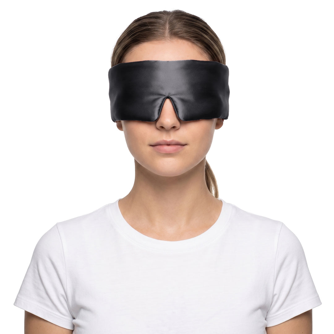 Woman wearing the black 3D contoured silk eye mask on a white background, the wide silk band covering both eyes and temples