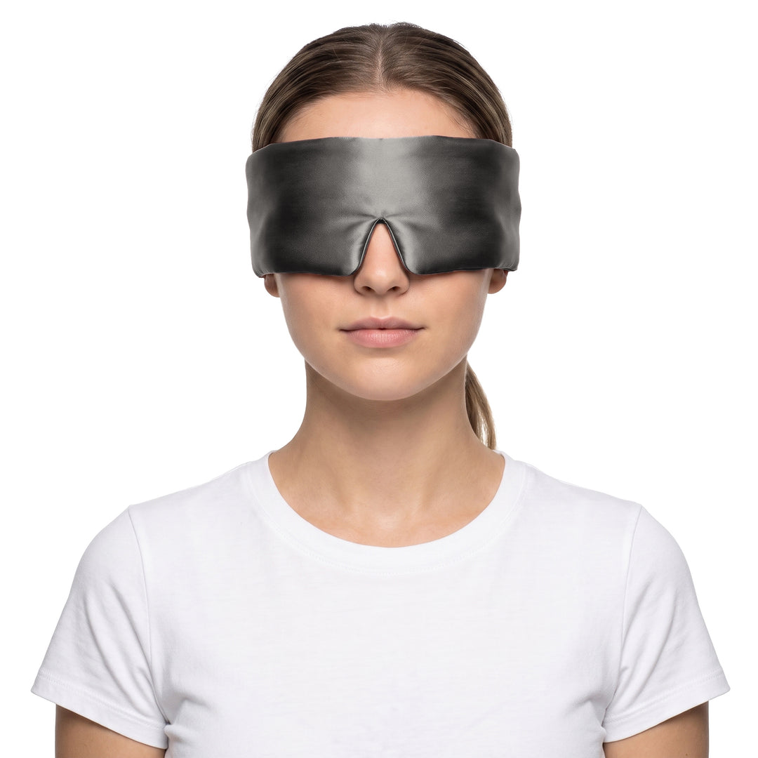 Woman wearing the charcoal 3D contoured silk eye mask on a white background, the wide silk band covering both eyes and temples