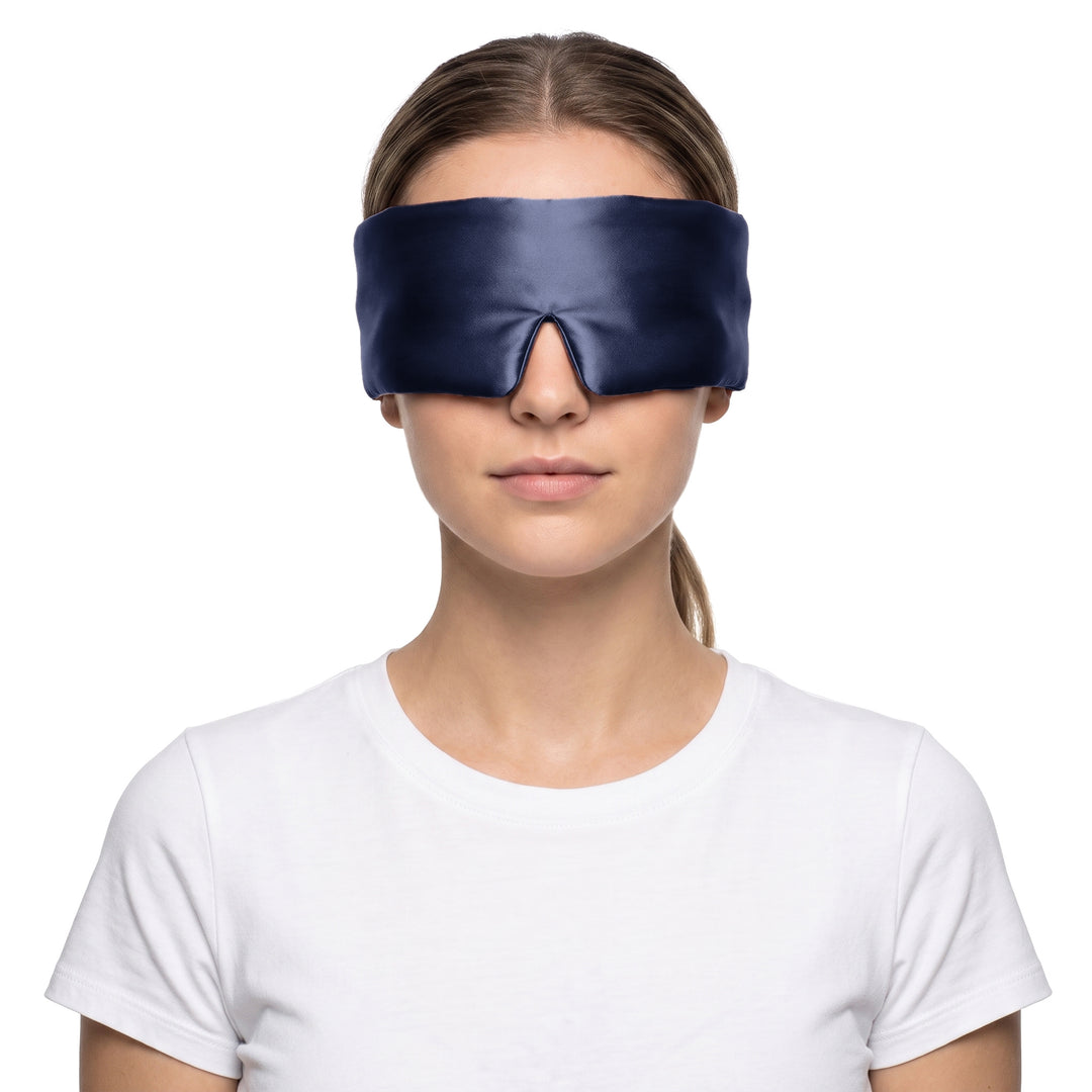 Woman wearing the navy blue 3D contoured silk eye mask on a white background, the wide silk band covering both eyes and temples