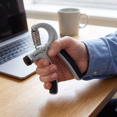 Hand grip strengthener held mid squeeze at a home office desk