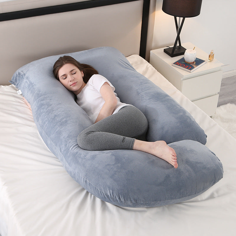 Grey J shaped pregnancy pillow on a bed with a woman resting inside it