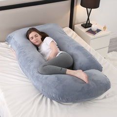 Grey J shaped pregnancy pillow on a bed with a woman resting inside it