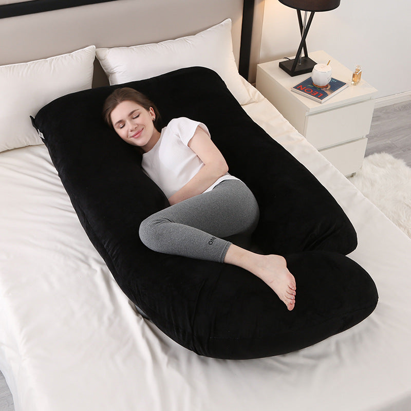 Charcoal black J shaped pregnancy pillow on a bed with a woman resting inside it