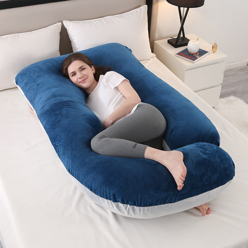 Navy and light grey J shaped pregnancy pillow on a bed with a woman resting inside it