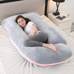 Pink and grey J shaped pregnancy pillow on a bed with a woman resting inside it