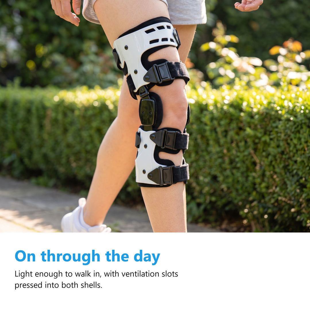 A woman walking outdoors wearing a white hinged knee brace on her knee