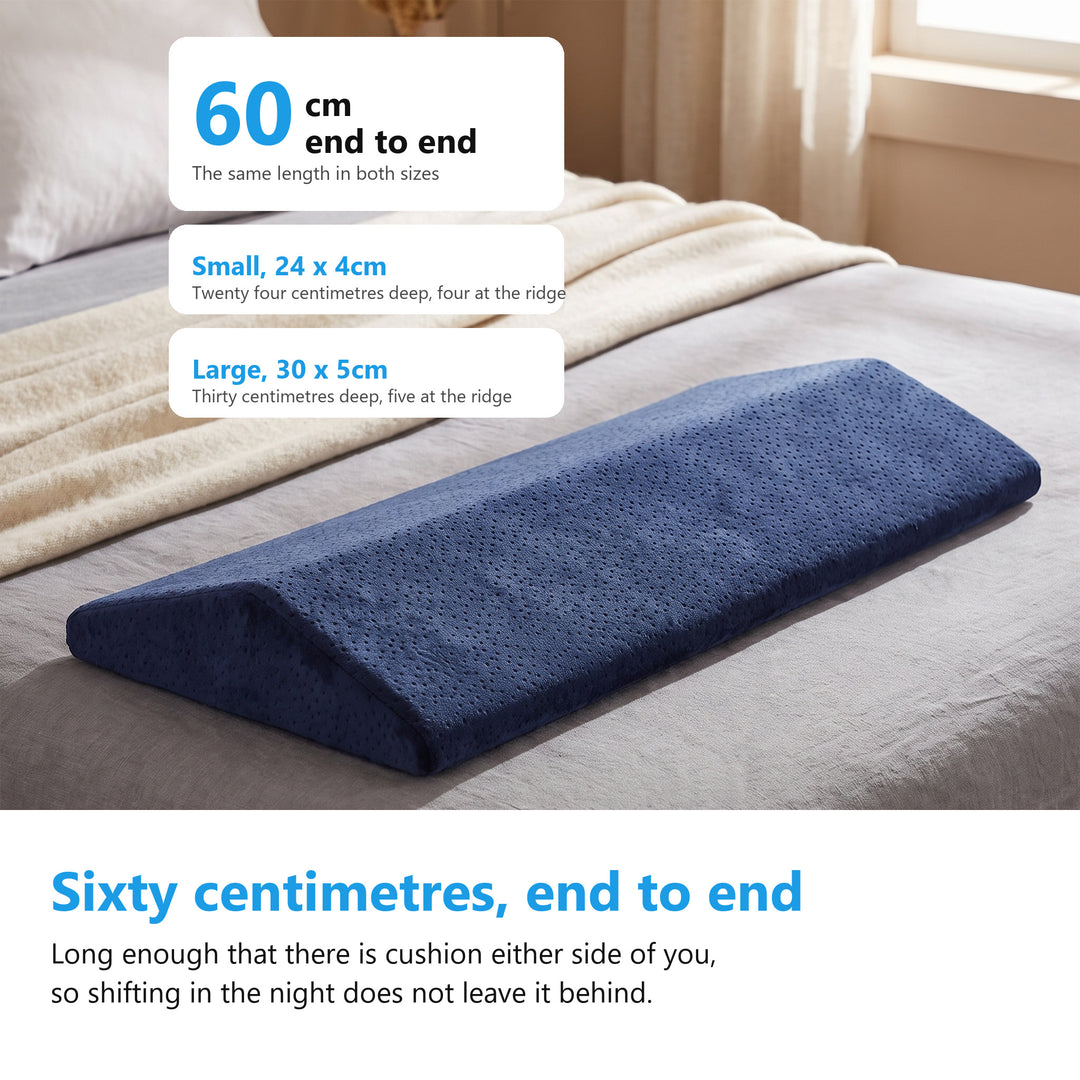 Navy velvet wedge cushion lying on a bed, labelled 60cm end to end with the small and large sizes beside it