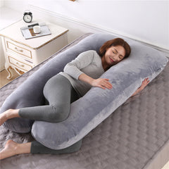 U shaped pregnancy pillow in dark grey velvet laid out on a bed