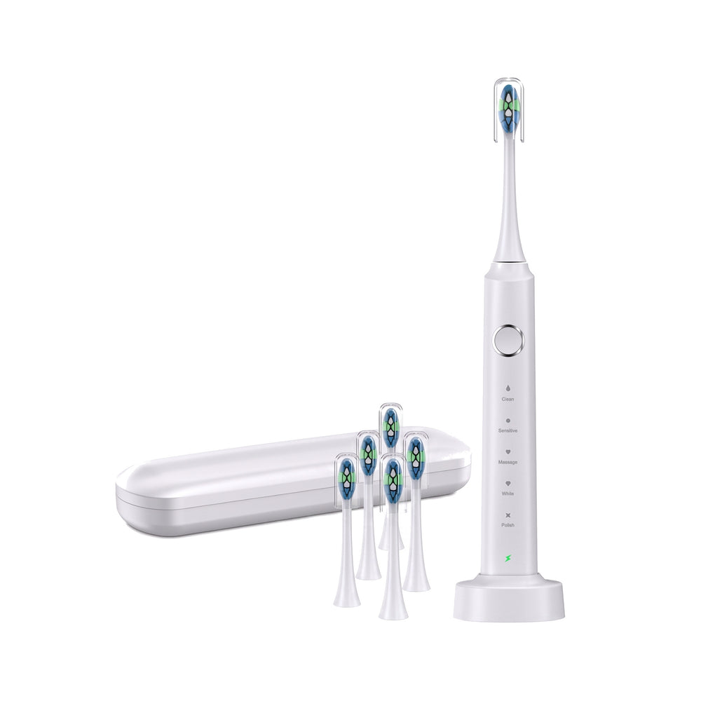 White electric toothbrush upright on its wireless charging base with its travel case and five spare brush heads on a white background