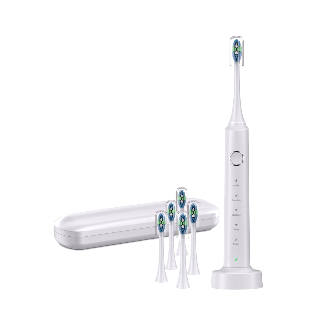 White electric toothbrush upright on its wireless charging base with its travel case and five spare brush heads on a white background