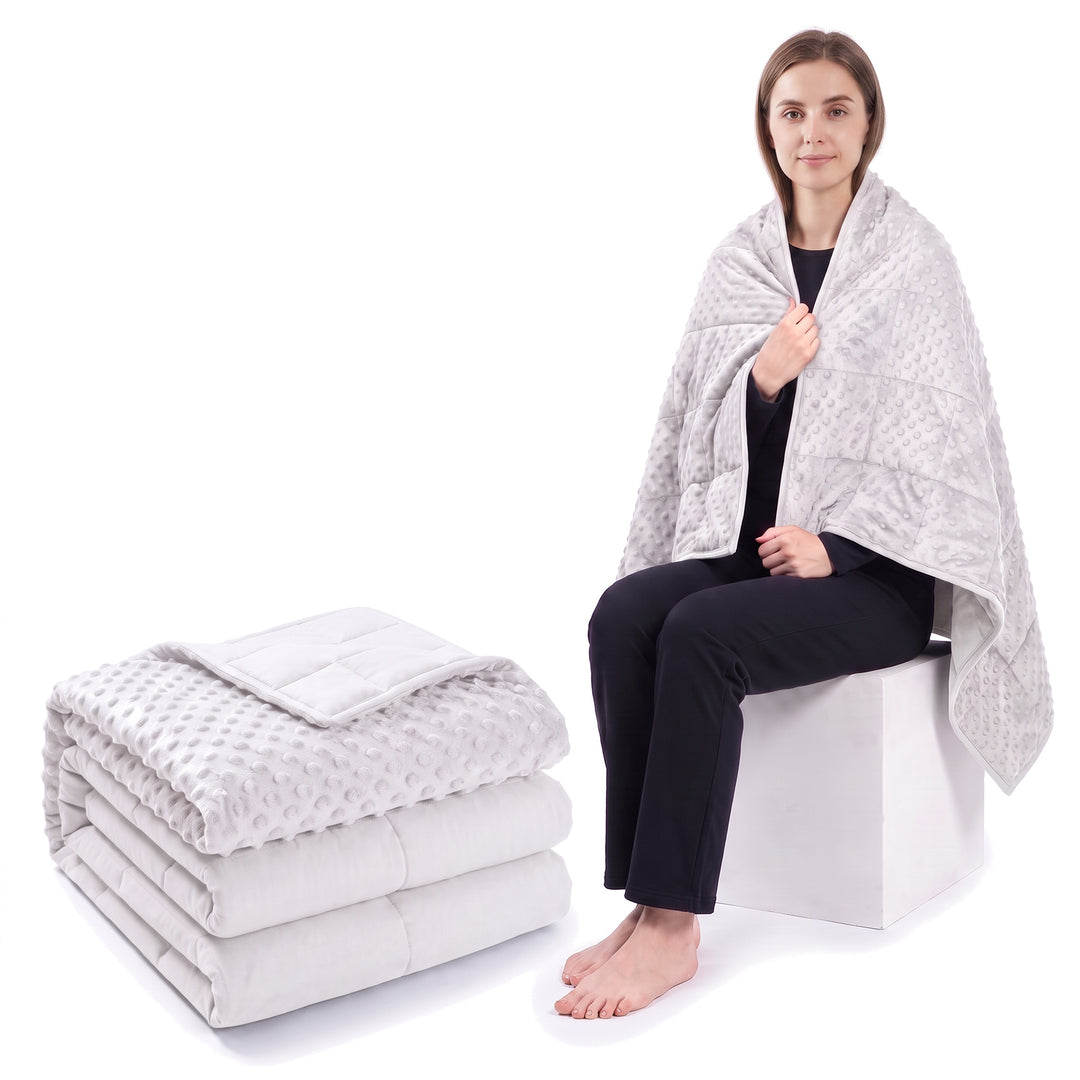 White weighted blanket folded on a white background beside a woman wrapped in the same blanket