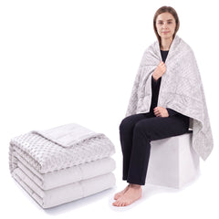 White weighted blanket folded on a white background beside a woman wrapped in the same blanket