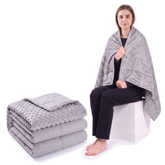 Light grey weighted blanket folded on a white background beside a woman wrapped in the same blanket