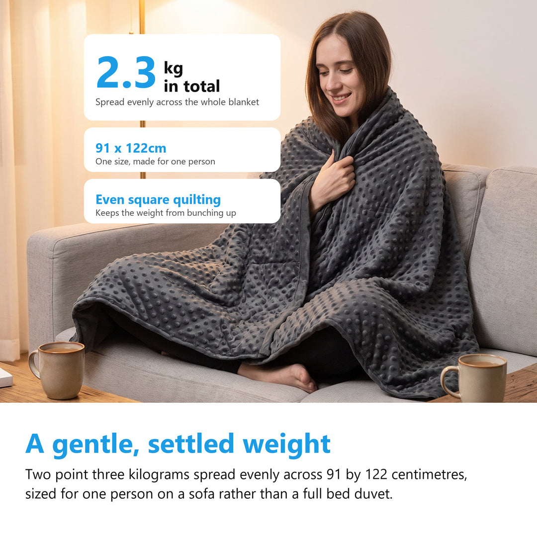 Woman on a sofa wrapped in a 2.3kg weighted blanket measuring 91 by 122cm